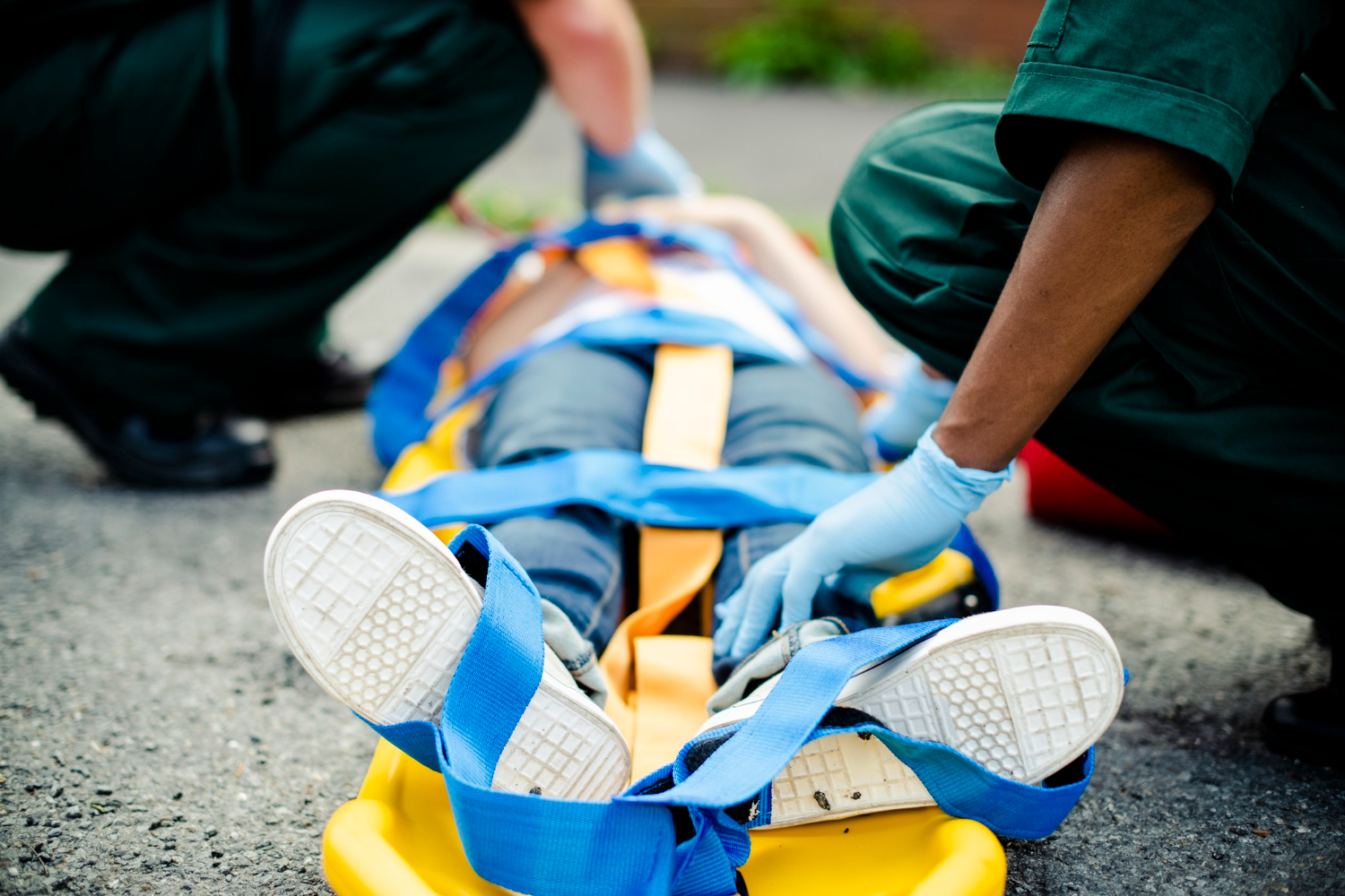 EMS professionals work on a patient strapped to a backboard resting on the ground.