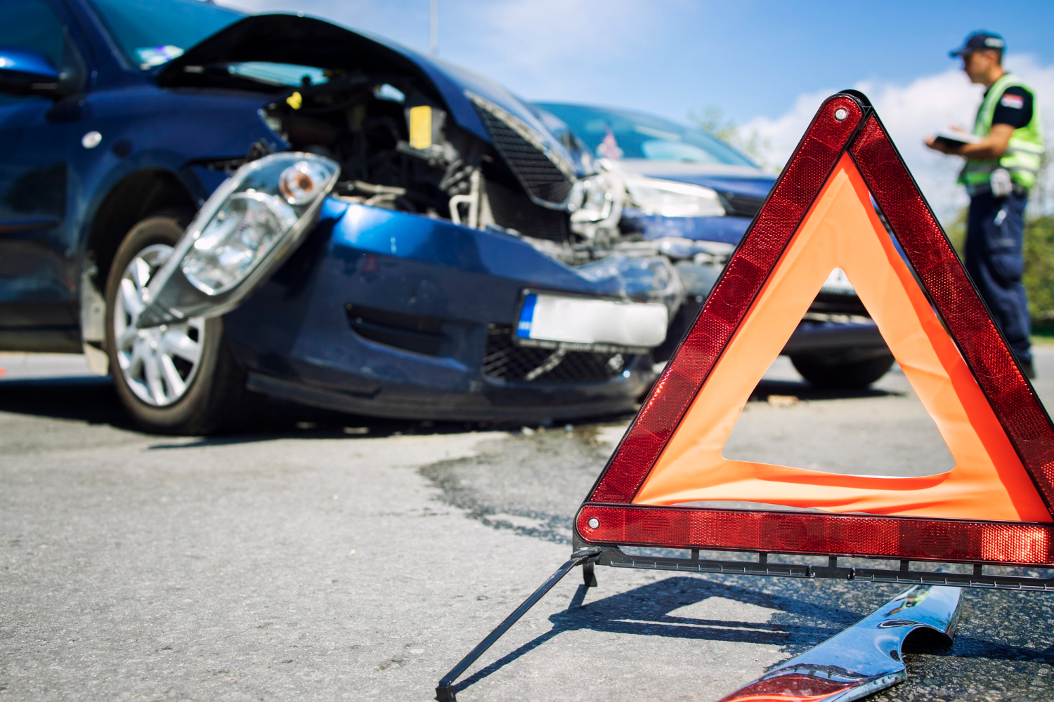 A caution triangle sits in front of a wrecked vehicle at the scene of a car accident.