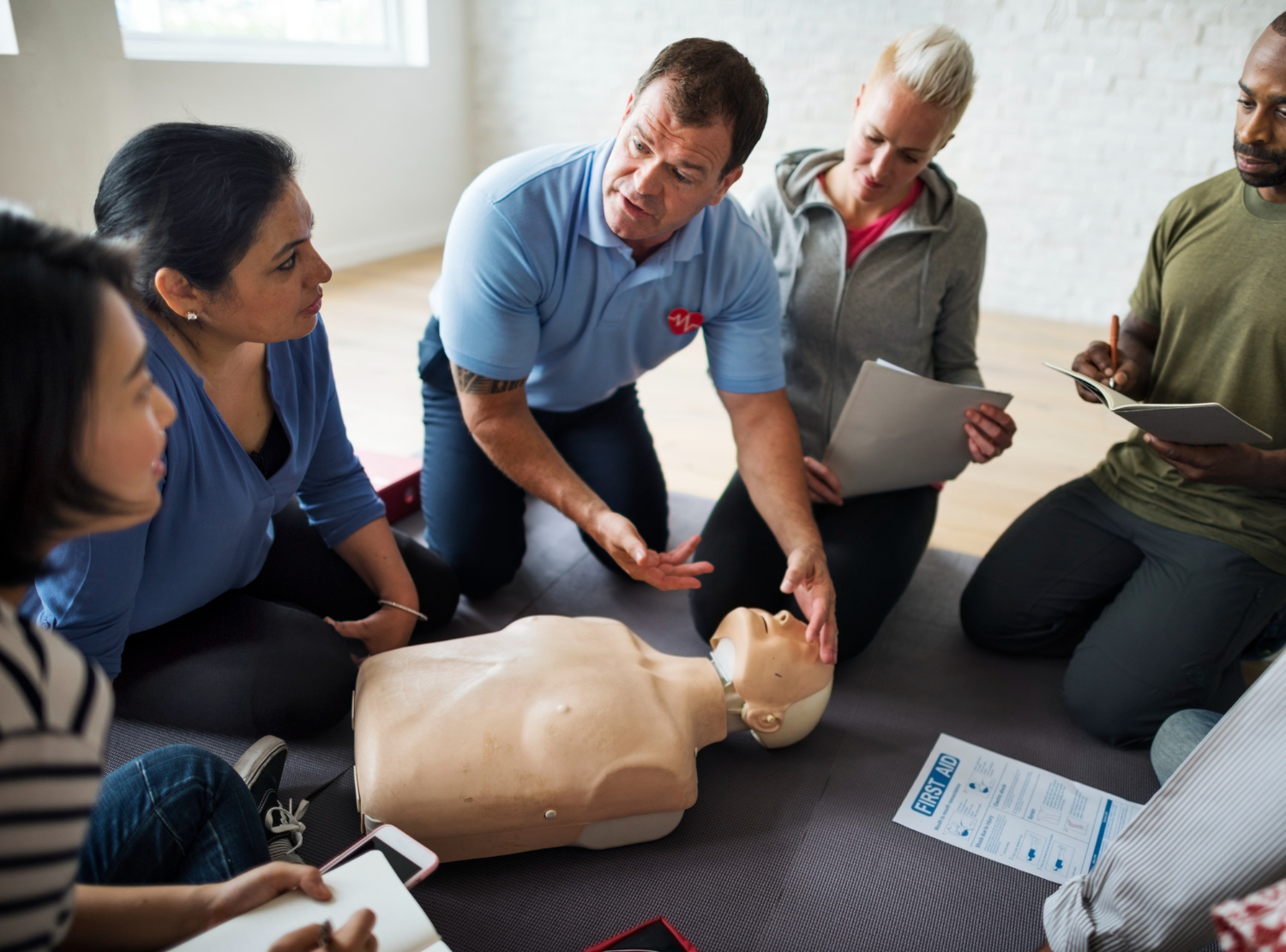 A male paramedic teaches a group of people how to perform CPR on a medical dummy.